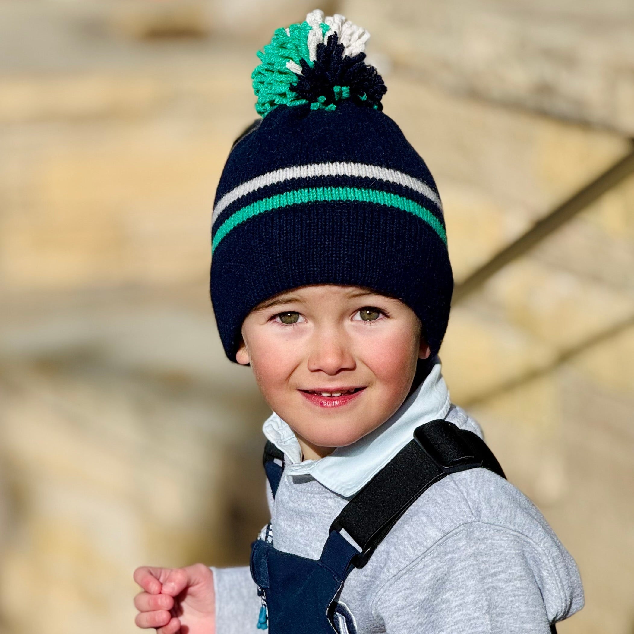 Child wearing a striped knit hat with a pom-pom, standing outdoors.